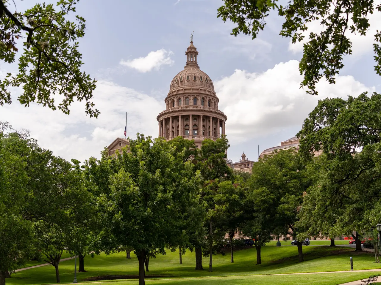 The pink granite dome of the Texas State Capitol in Austin, rising above live oaks on the Capitol grounds