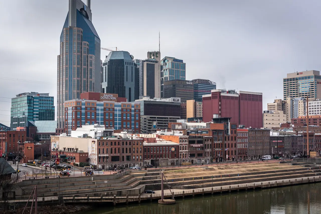 Downtown Nashville from across the Cumberland River, with the twin-spired AT&T "Batman" Building above the brick storefronts of Lower Broadway and the Riverfront Park steps
