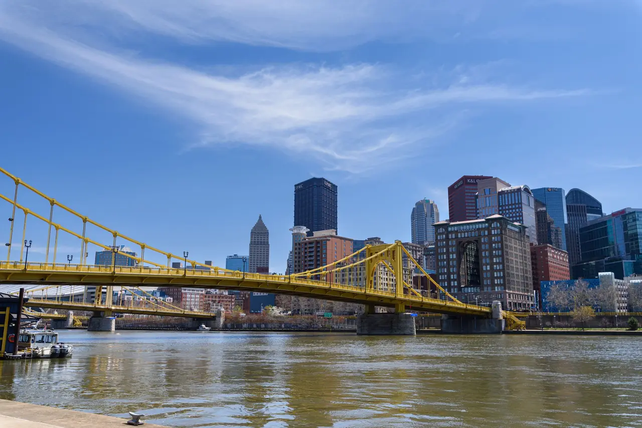 One of Pittsburgh's yellow Three Sisters bridges crossing the Allegheny River toward downtown on a blue-sky day